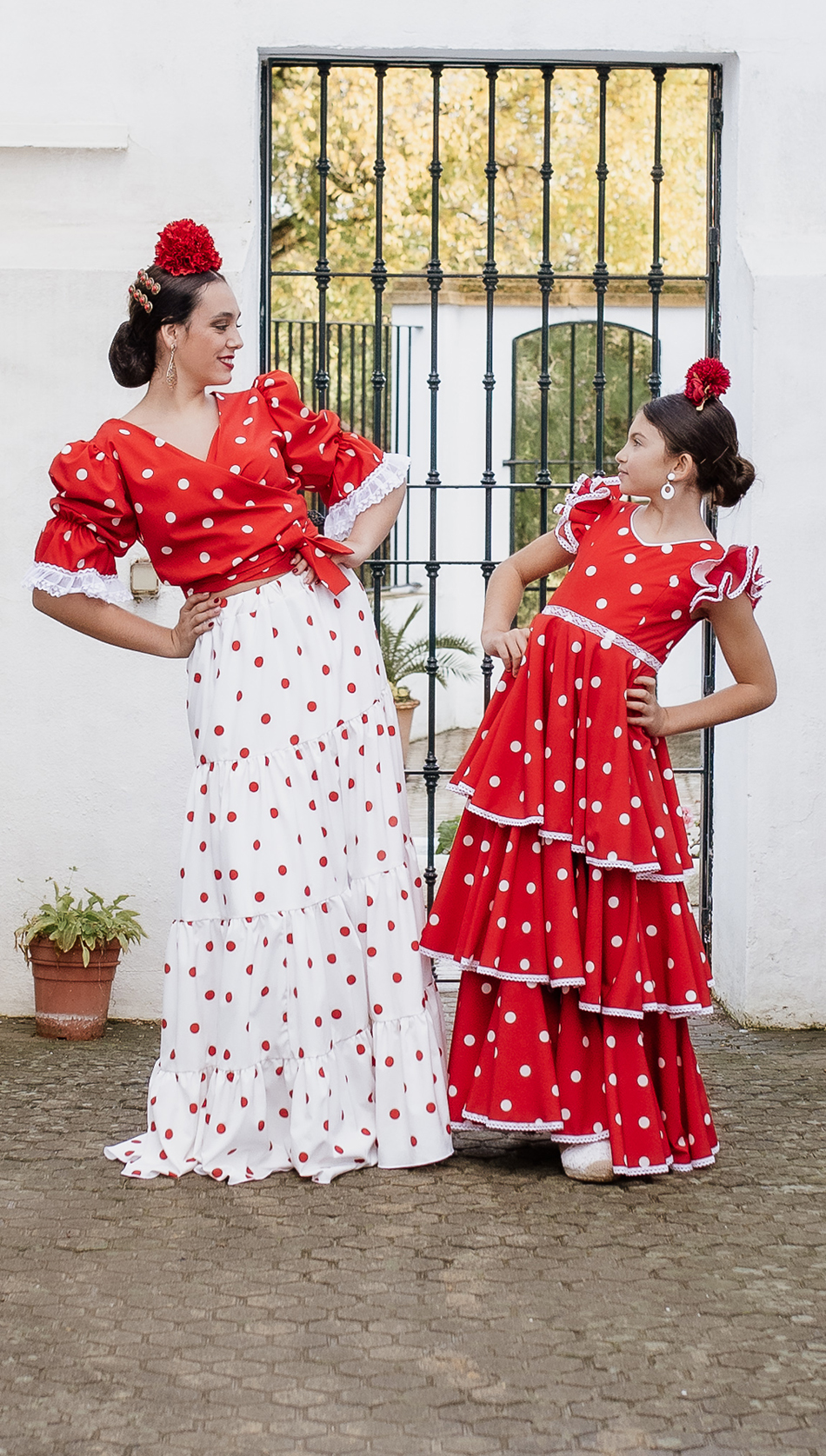 Mujer y ni&ntilde;a vestidas con trajes de flamenca rojos de la colecci&oacute;n Carmen Garrido en un patio andaluz de Granada.