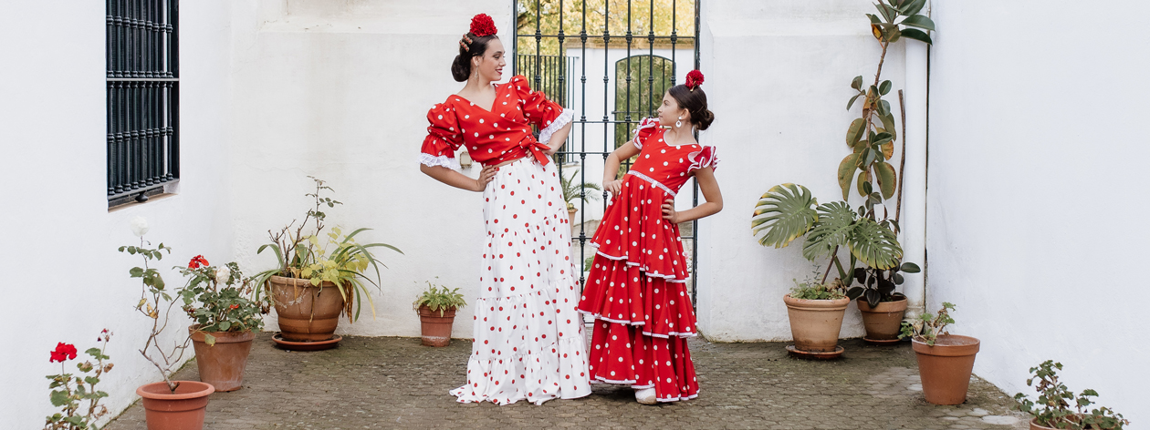 Mujer y ni&ntilde;a vestidas con trajes de flamenca rojos de la colecci&oacute;n Carmen Garrido en un patio andaluz de Granada.